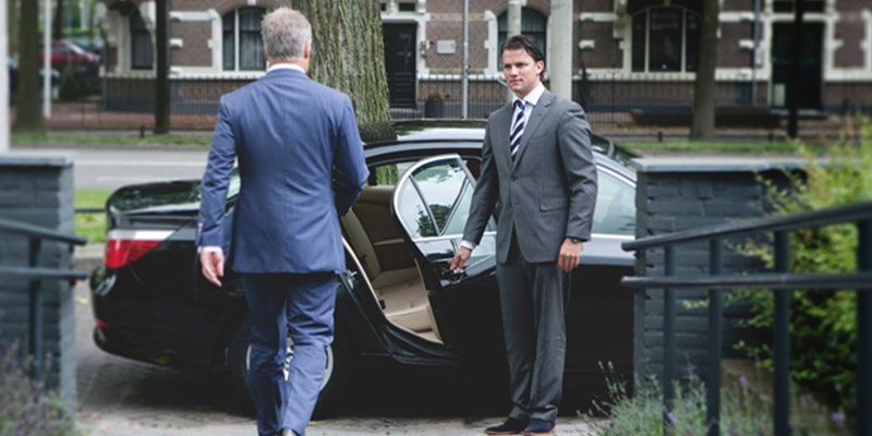 Chauffeur en costume accueillant son client en lui ouvrant la porte de son véhicule noir